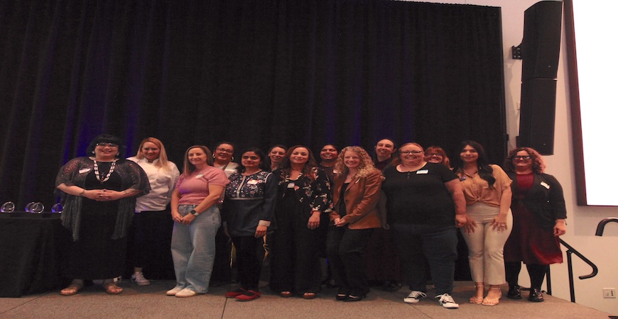 Thirteen women's luncheon honorees pose for a picture together on a stage.